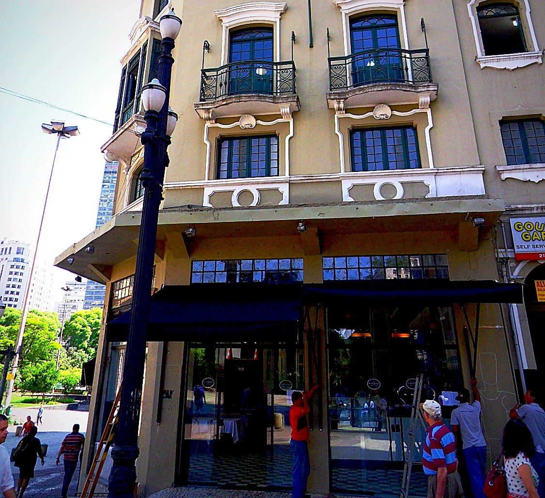 Fachada do edifício com o térreo do restaurante, toldos pretos e portas de vidro