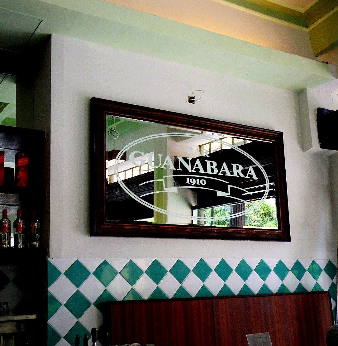 Espelho com o logotipo “Bar Guanabara 1910” sobre azulejos verdes e brancos