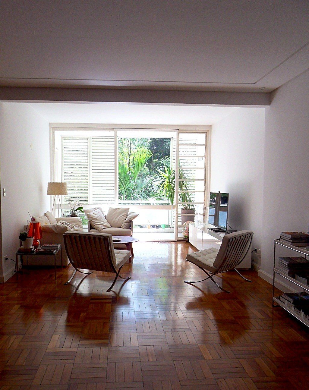 Sala de estar com poltronas Barcelona e caixilho original aberto para as árvores