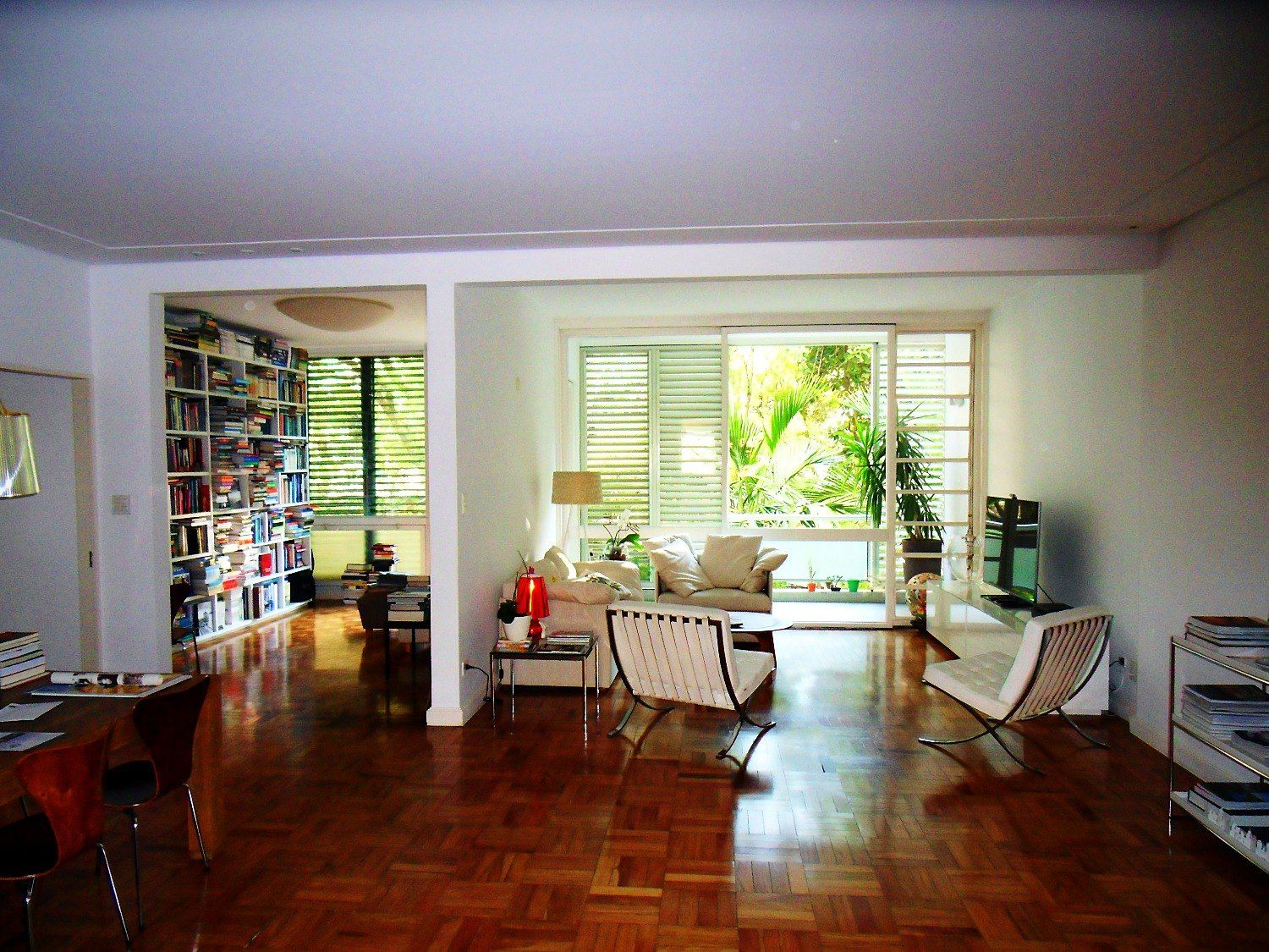 Sala integrada à biblioteca, tacos de peroba e caixilhos originais para o jardim