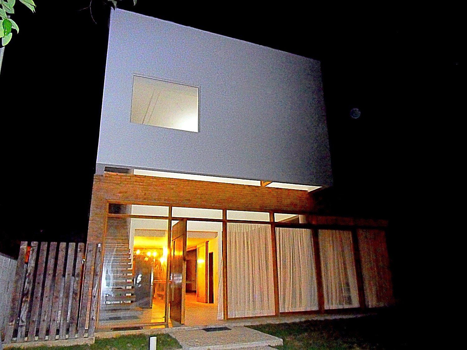 Fachada frontal à noite, com o interior iluminado atrás dos caixilhos de madeira