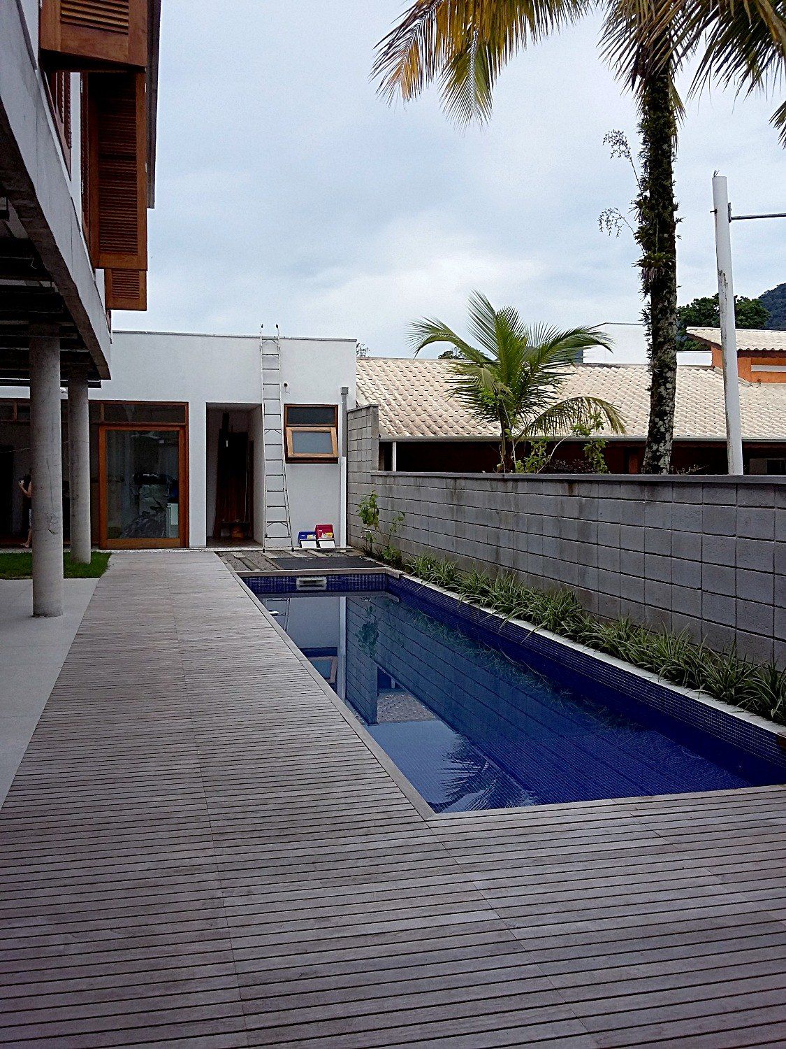 Deck de madeira ao longo da piscina, sob o pavimento superior com venezianas