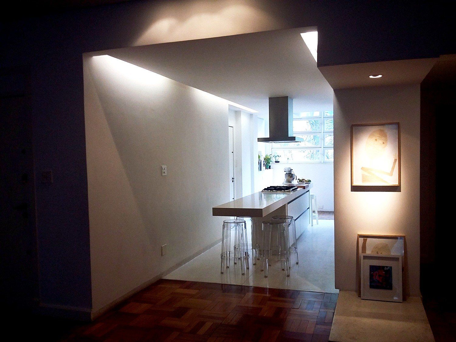 Abertura da cozinha para a sala, com bancada, banquetas e iluminação embutida