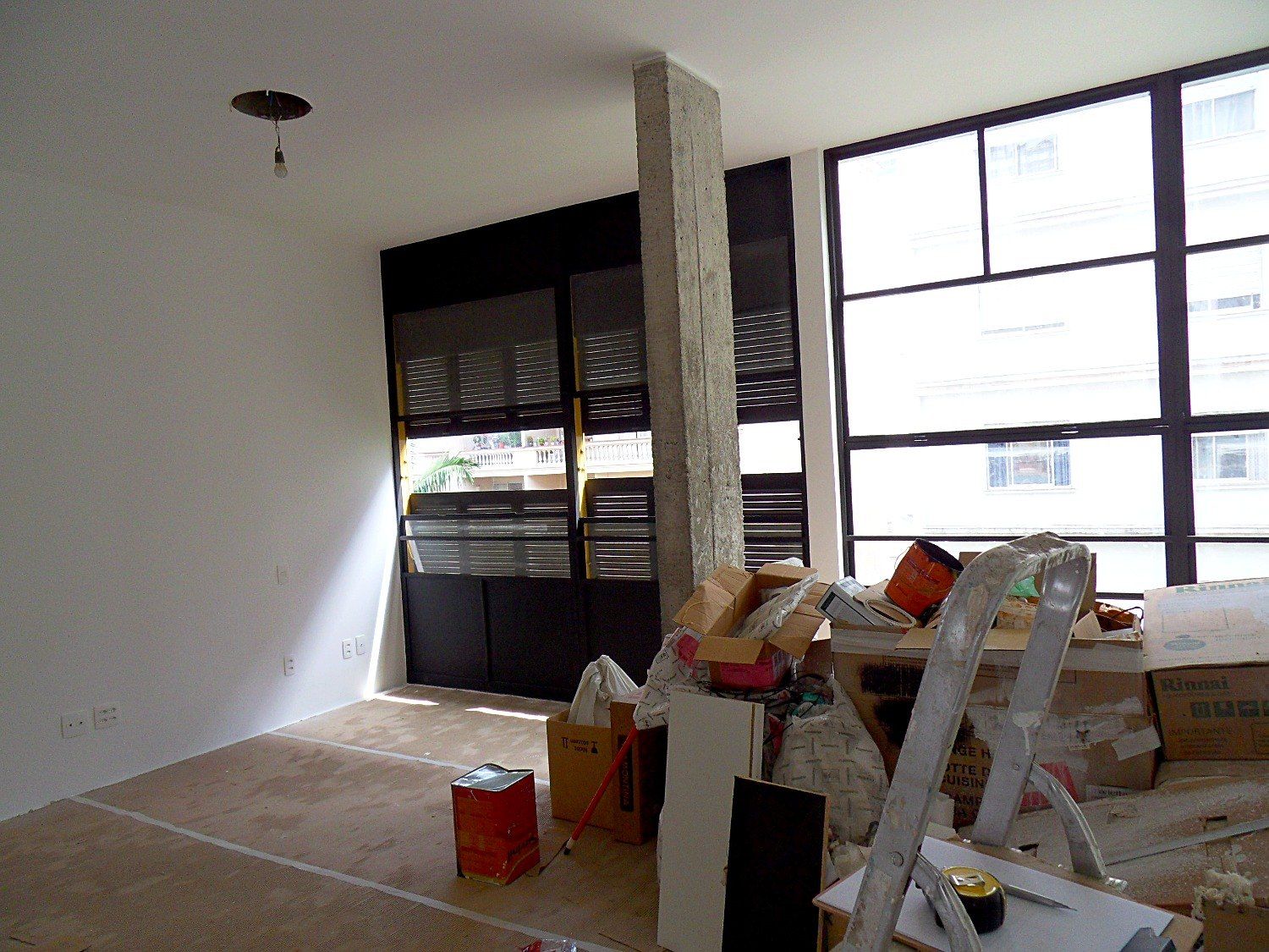 Sala integrada com venezianas e caixilhos pintados de preto e pilar de concreto aparente
