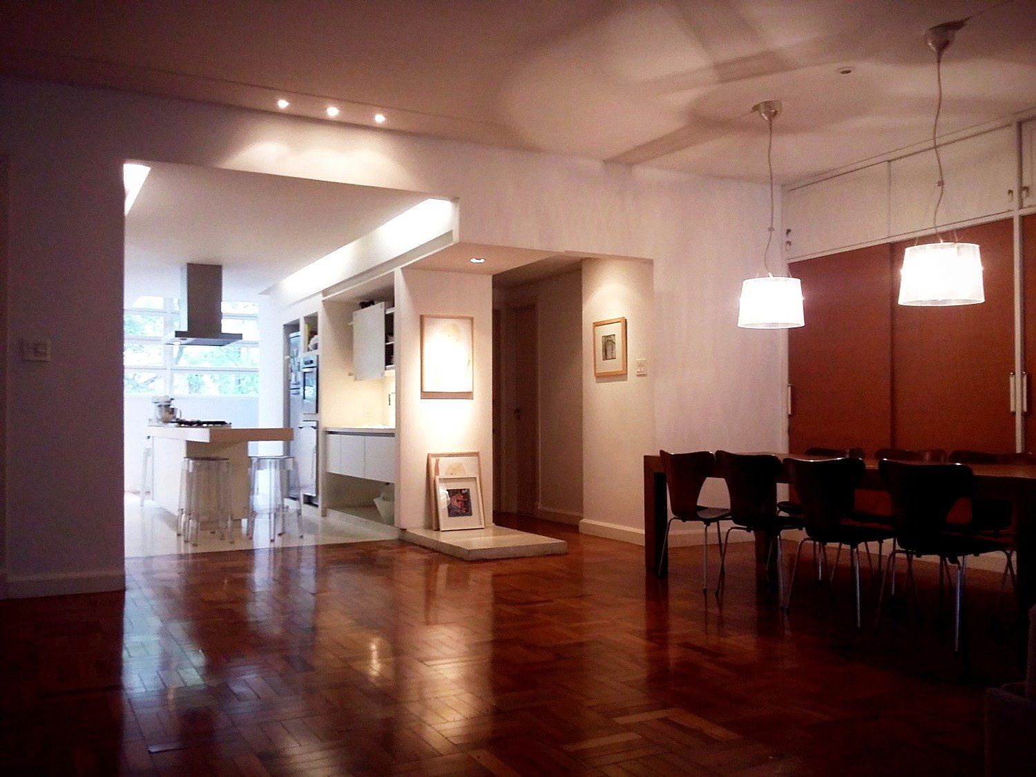 Sala de jantar com pendentes e armário de madeira, cozinha aberta ao fundo
