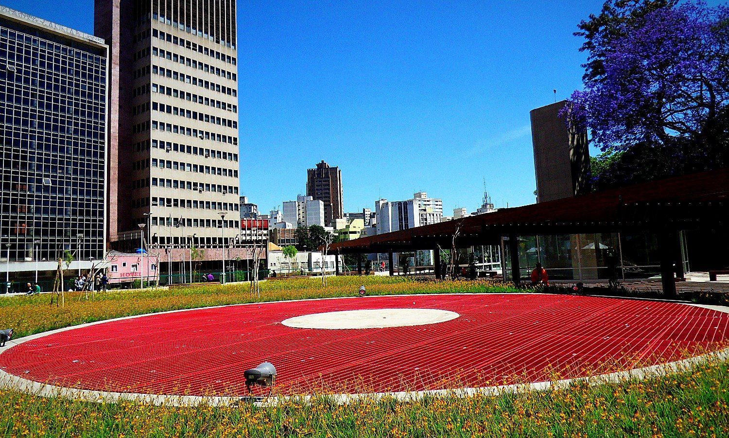 Esplanada com o grande disco vermelho e o pergolado ao fundo