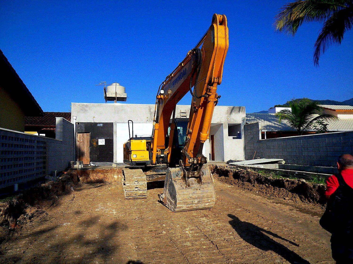 Escavadeira no terreno durante a demolição e preparo do lote